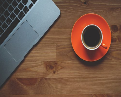 A well lit modern office desk with a cup of coffee and a notebook